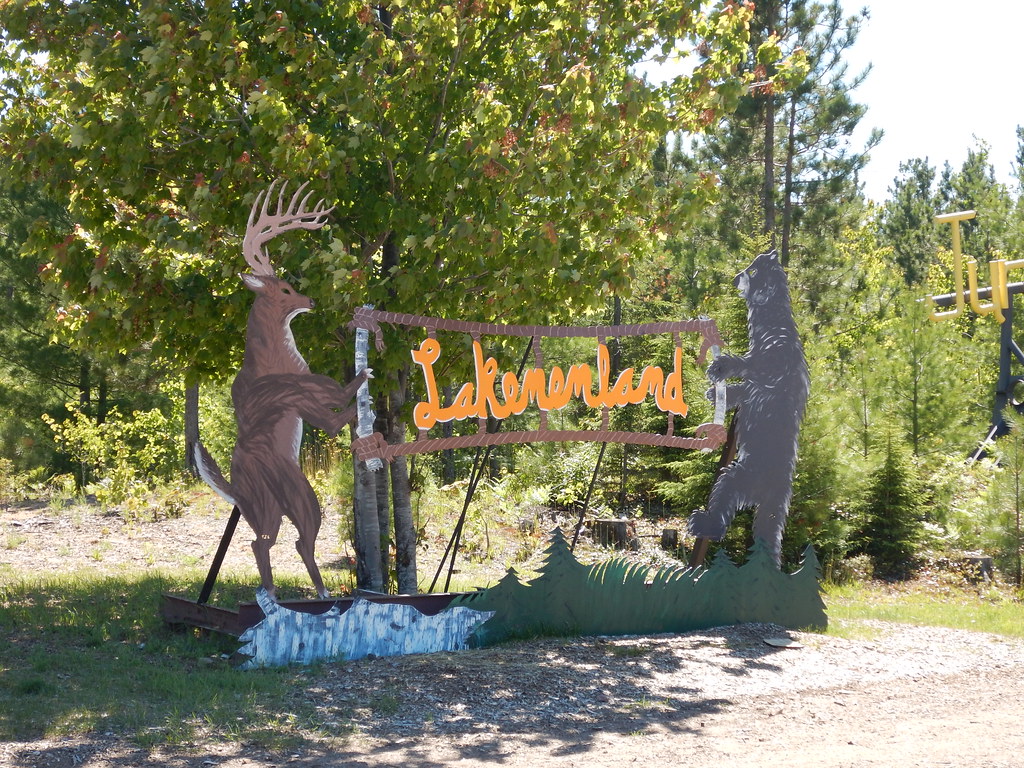 Picture of the entrance sign to Lakenenland Sculpture park. This sculpture, made of metal, has a deer standing on its back legs holding the sign on the left and a bear on its back legs holding the sign on the right.